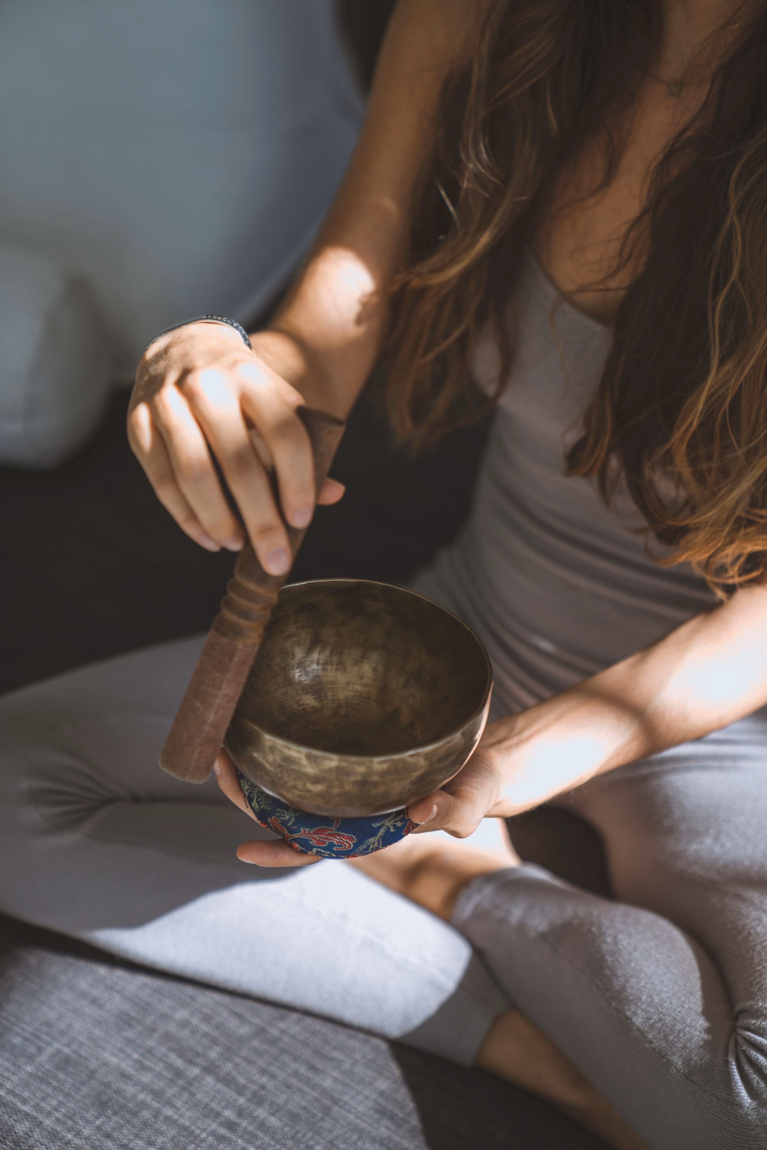A person playing a brass singing bowl with a wooden mallet, seen from behind.