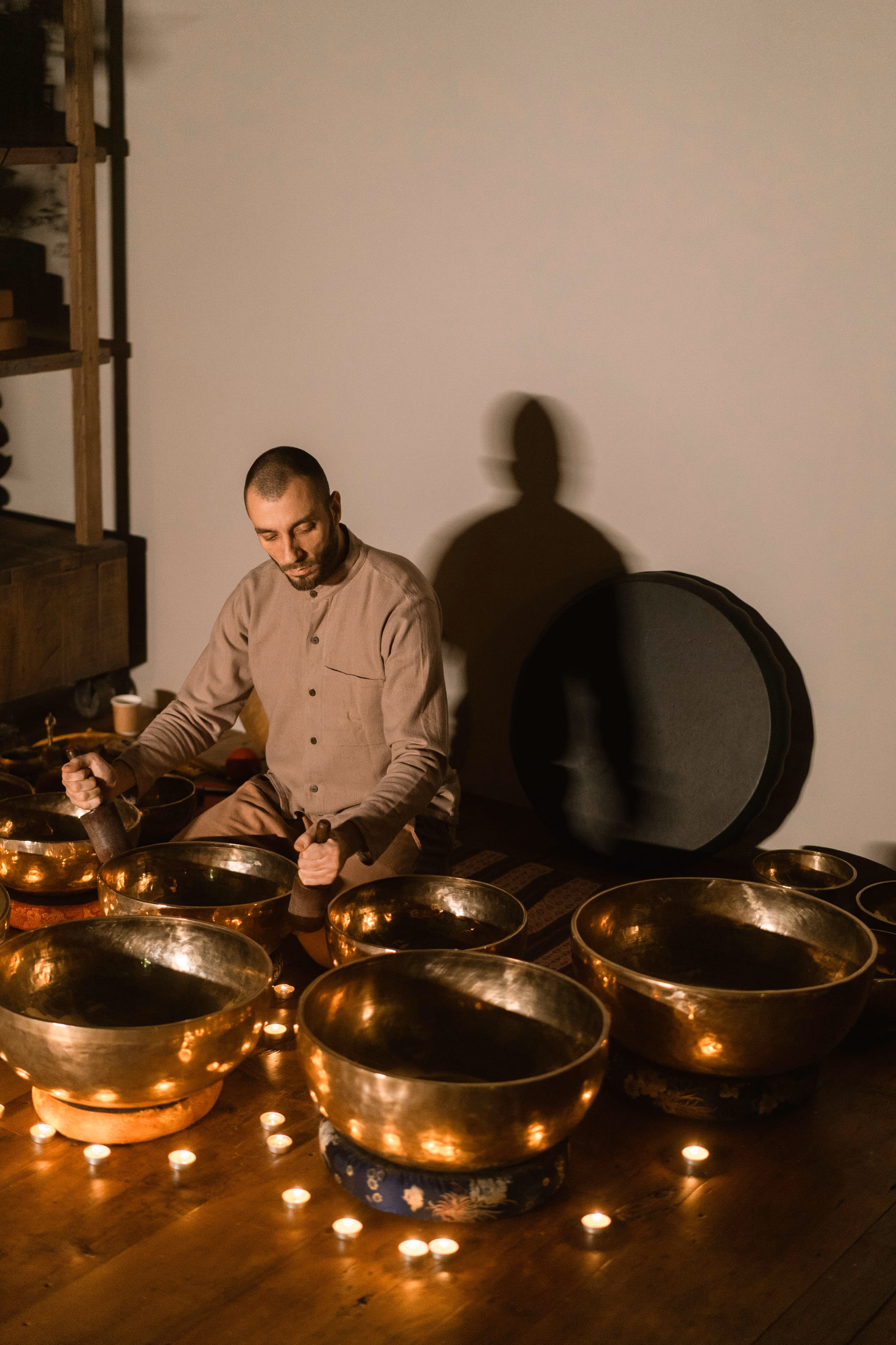 Brass singing bowls and a frame drum arranged on a warm wooden floor.