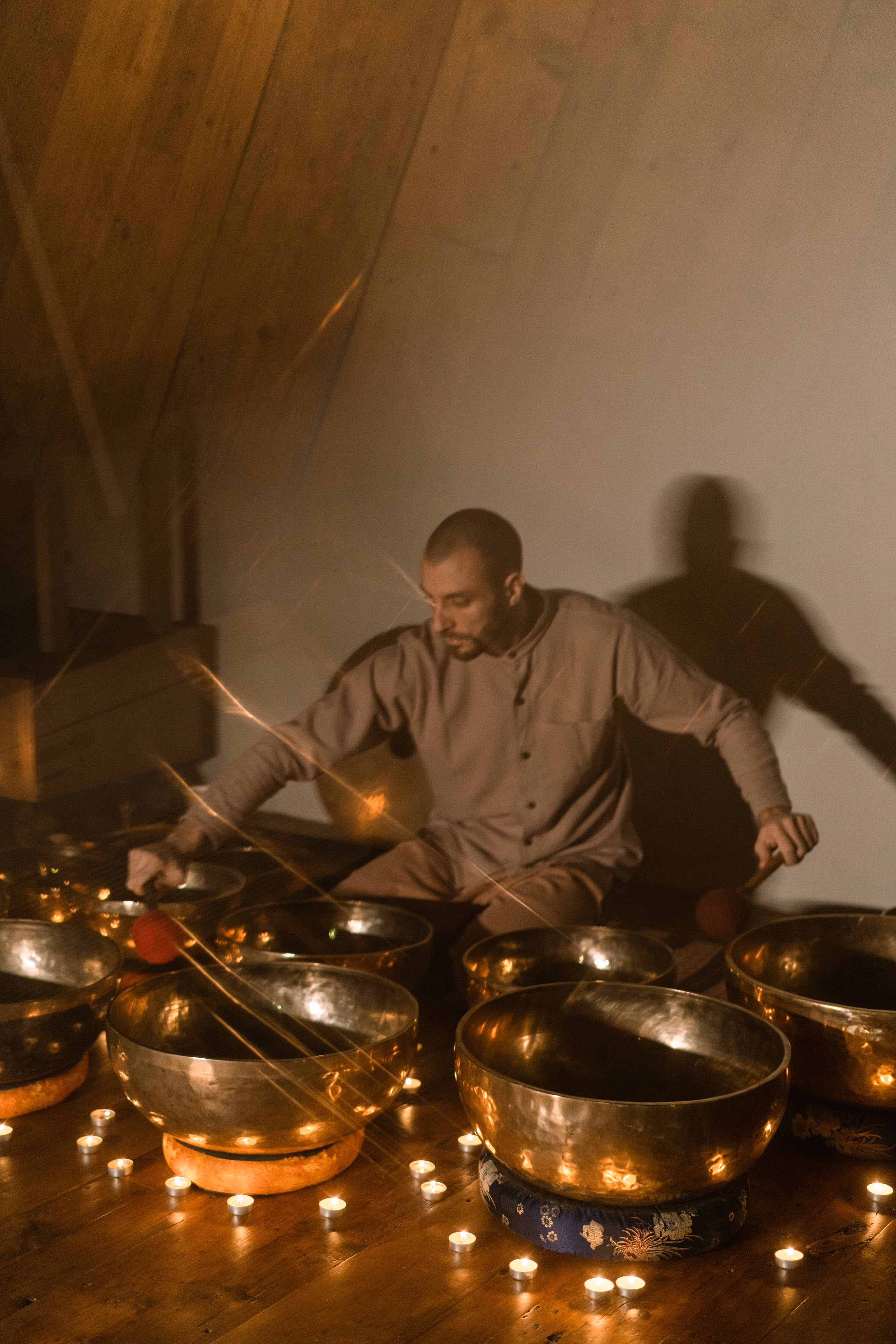 Brass singing bowls ringed by small lit candles, with the light of a moving mallet trailing across the frame.