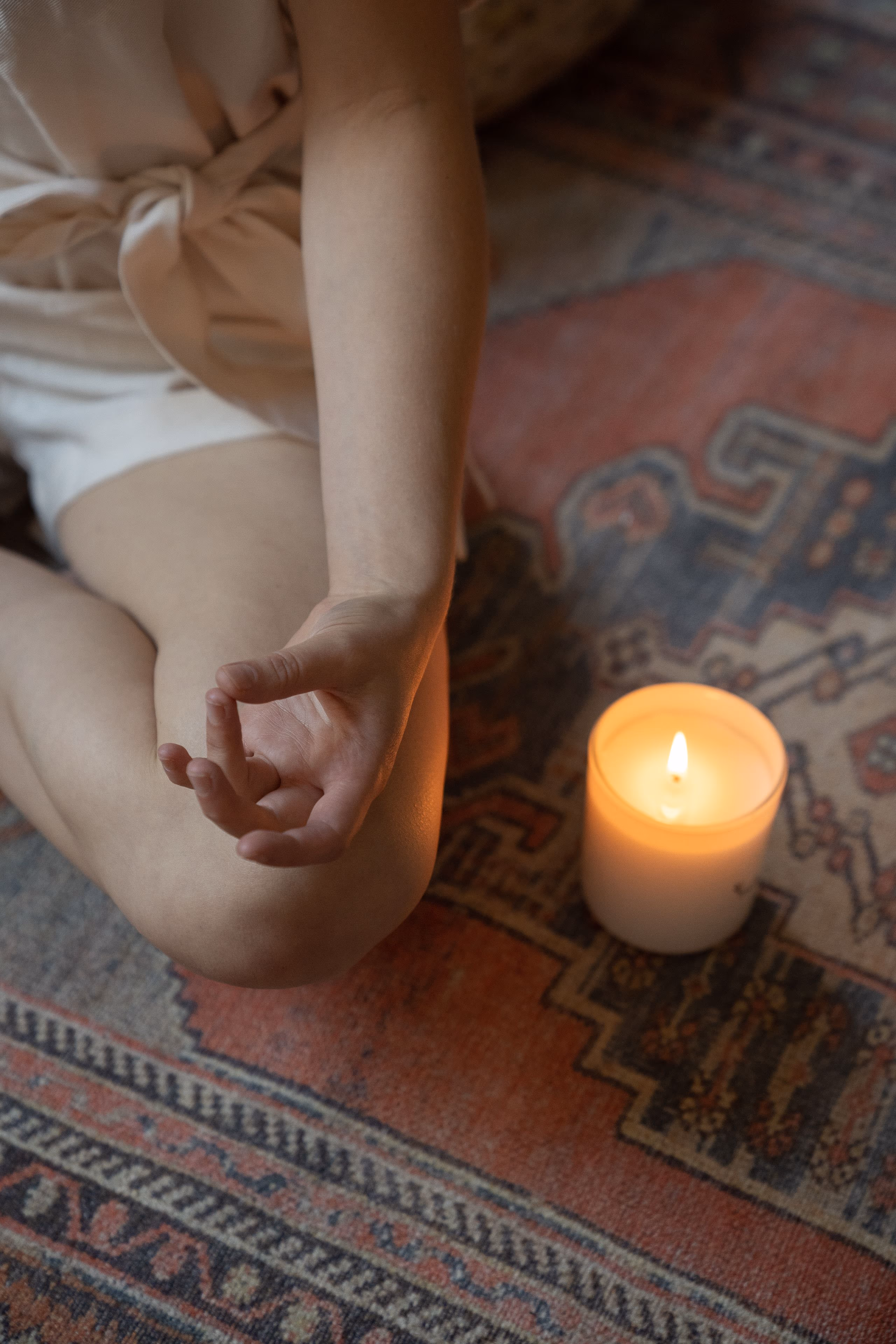 A pair of hands resting open beside a single lit candle on a warm floor.