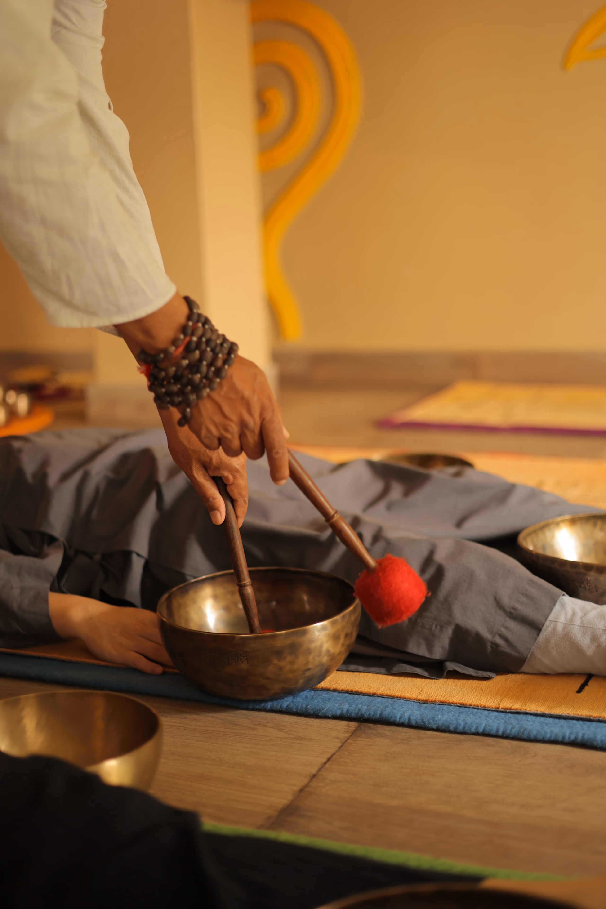 A hand playing a small singing bowl resting on someone's body as they lie down.