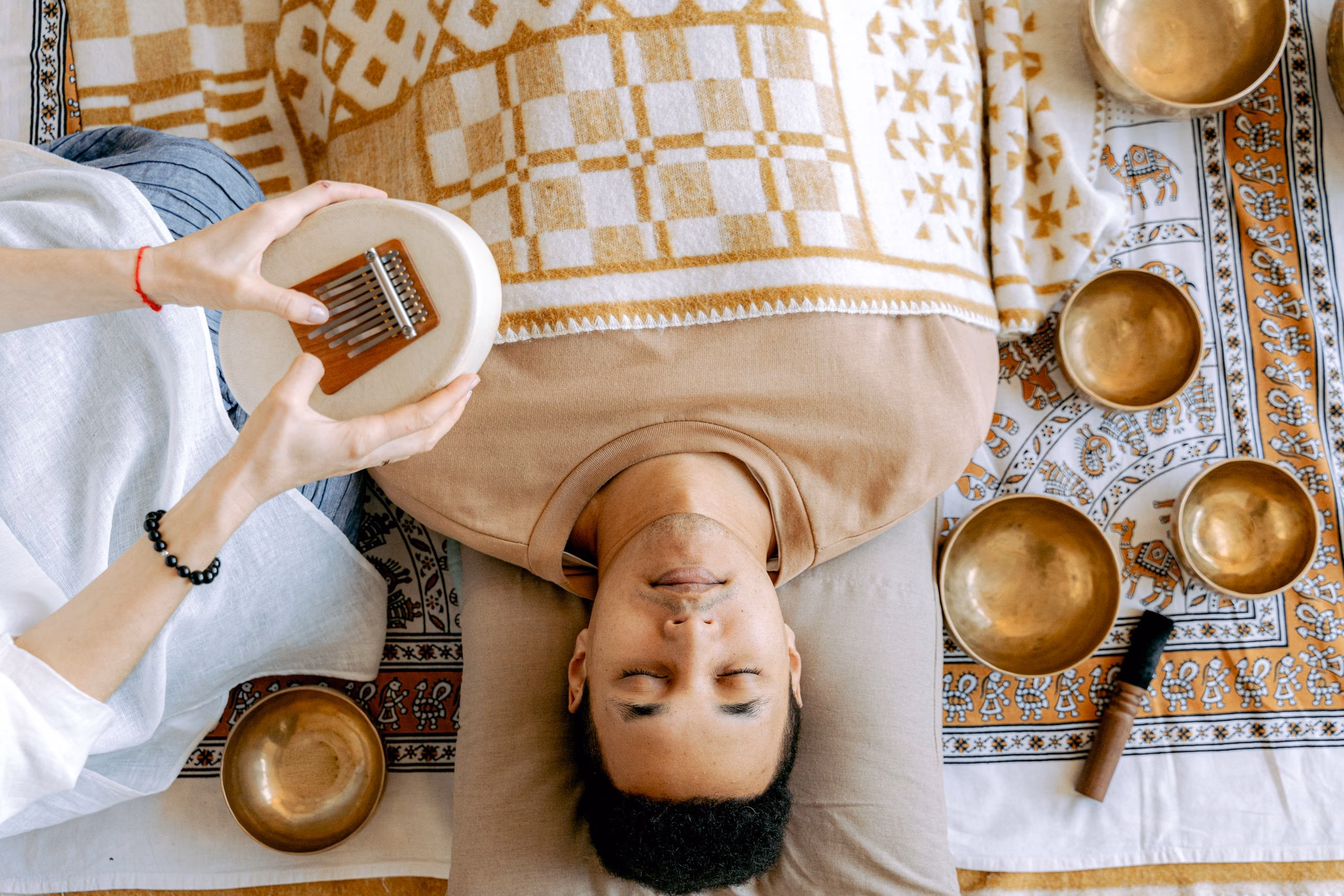 Someone lying still with their eyes closed on warm gold and cream blankets, seen from above.