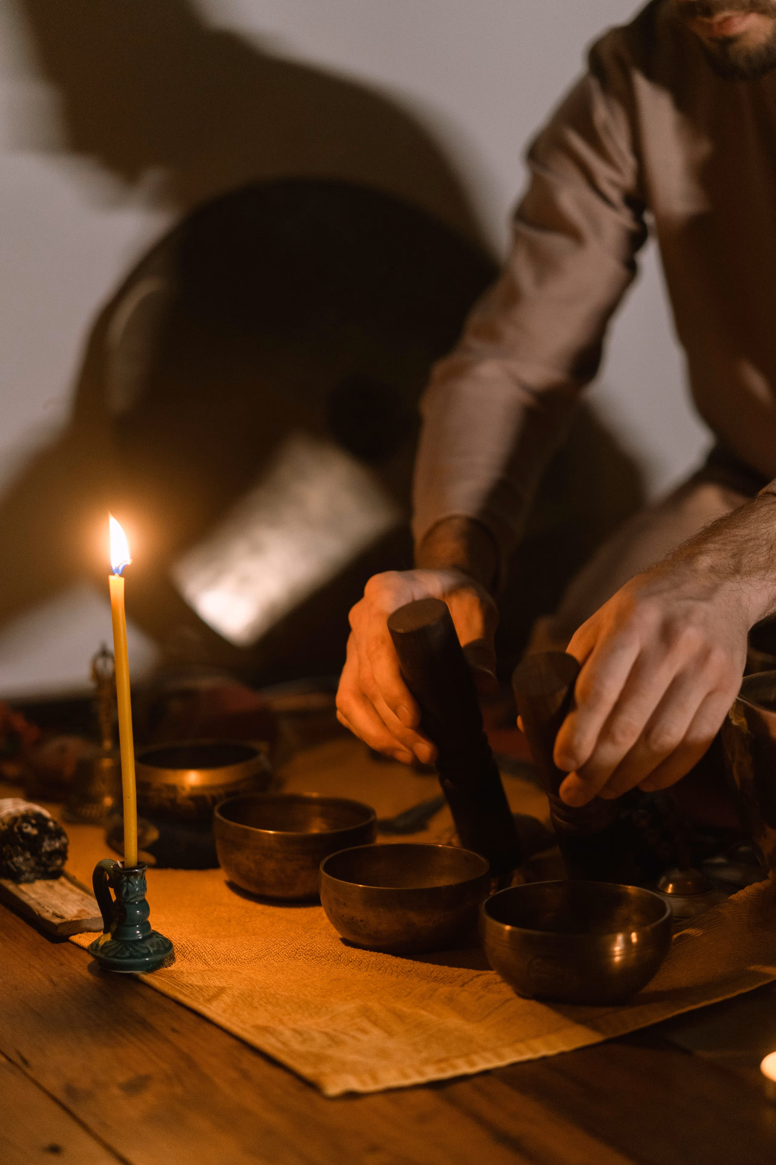 Hands resting over a pair of small singing bowls beside a lit taper candle.