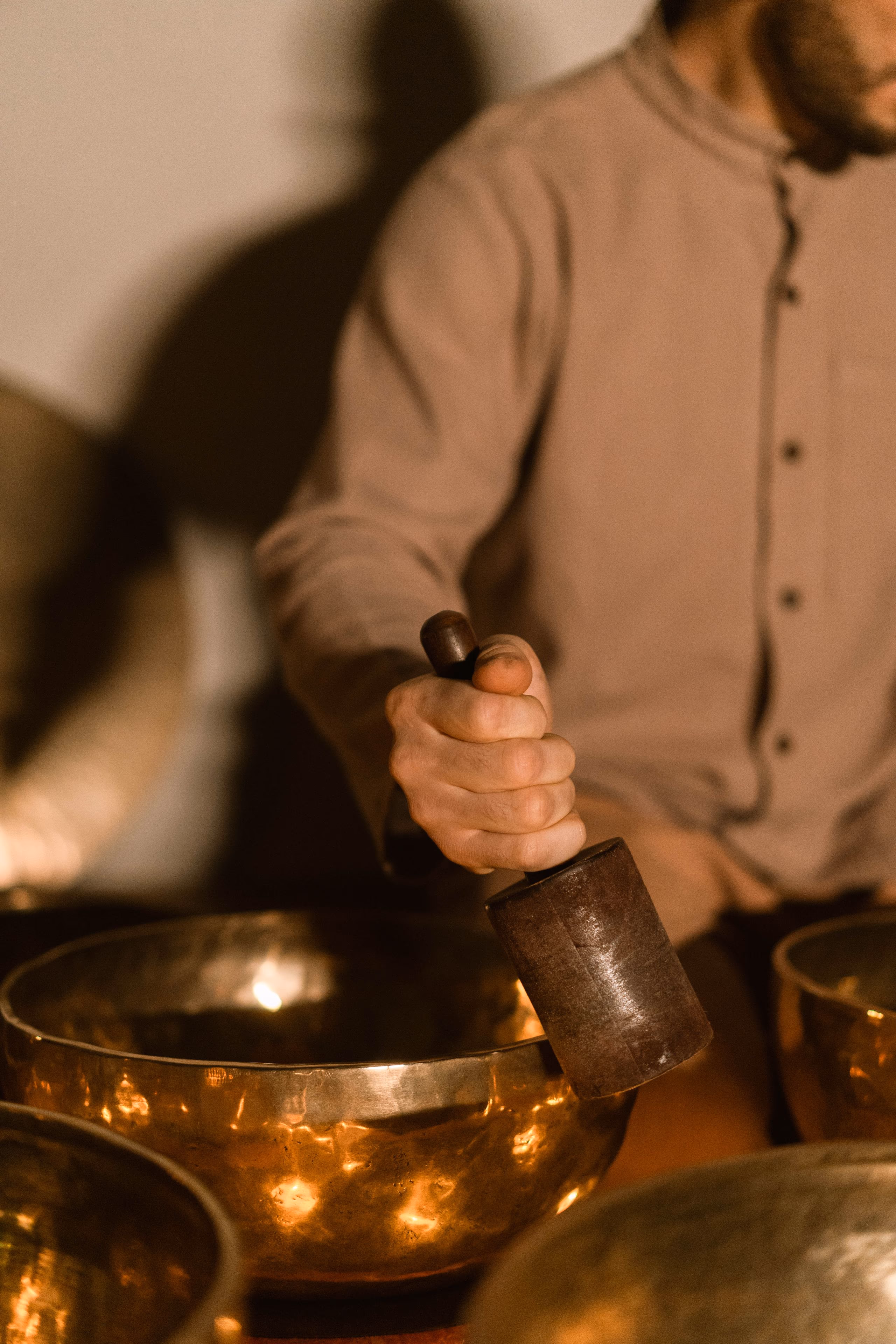 Two hands circling a wooden mallet around the rim of a brass singing bowl.