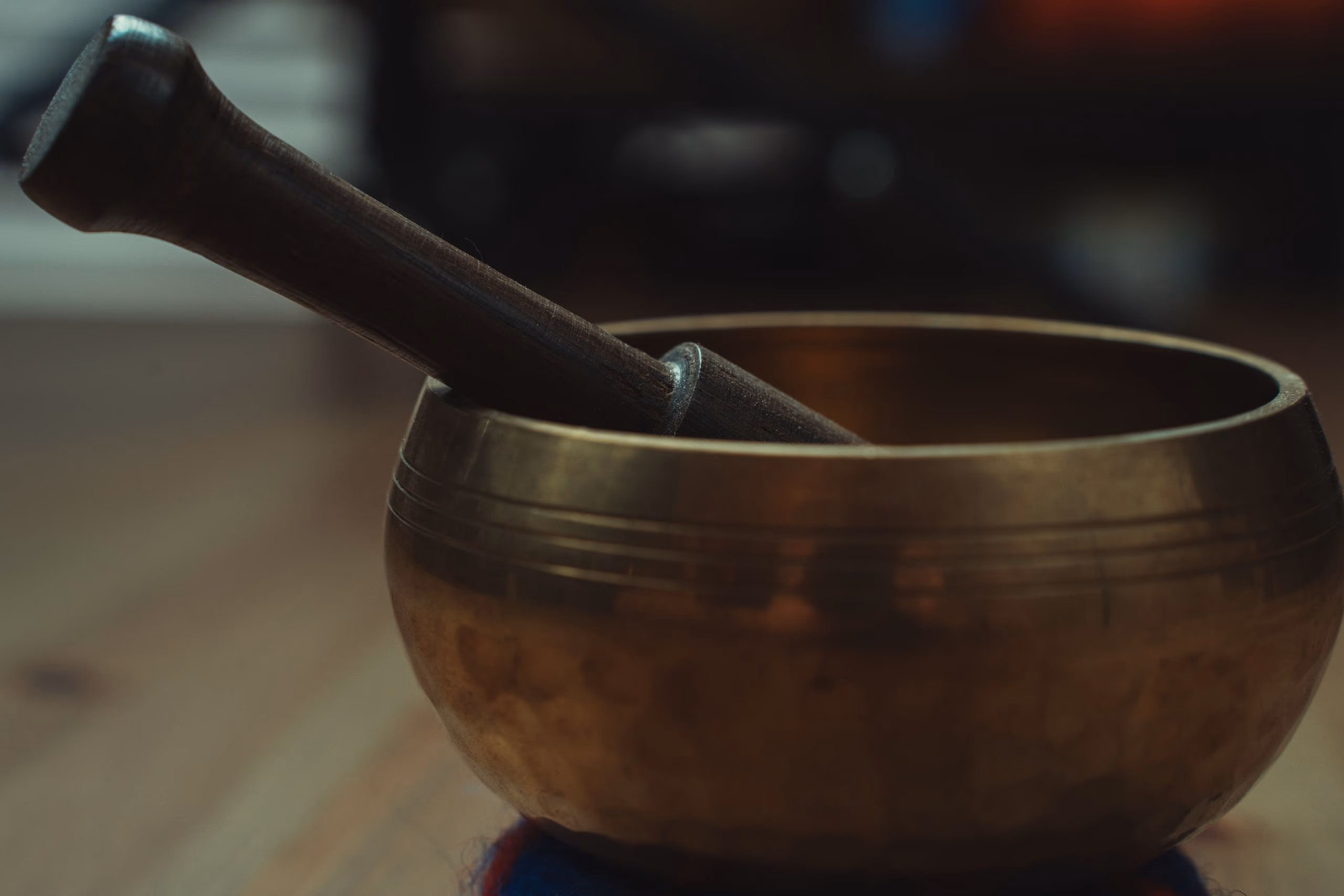 A single brass singing bowl with its mallet resting inside, lit against a dark background.
